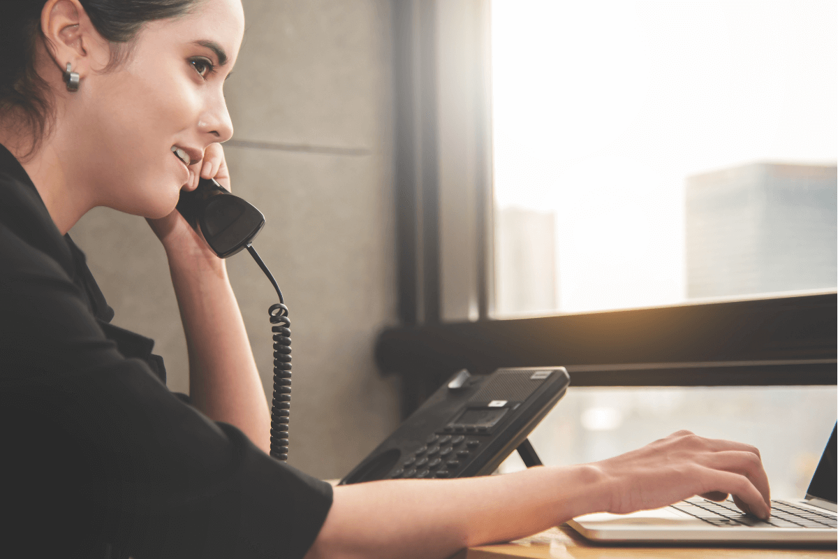 Female employee using laptop on desk while answering telephone call